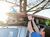 Man fastening paddleboard to roof of car