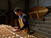 Mann mit Papier und Bleistift bei der Arbeit steht über Paddleboard aus Holz in der Werkstatt