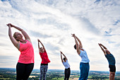 Gruppe von Frauen und Männern bei einem einem Yoga-Kurs auf einem Hügel