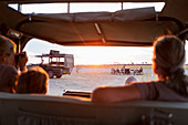 Family in safari vehicle taking photographs of a safari picnic at sunset.