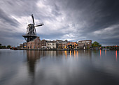 Blick auf die Windmühle De Adriaan, die sich während der Goldenen Stunde im Kanal des Flusses Spaarne spiegelt, Haarlem, Amsterdamer Bezirk, Papentorenvest, Randstad, Nordholland, Niederlande, Europa