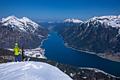 Snowboarder stehend mit Splitboard im Tiefschnee und Ausblick auf den Achensee und Gebirge im Frühjahr, Tirol, Österreich