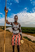Kara tribe man with elaborate chalk painting on his body, with the Omo River behind, Dus, Omo Valley, Ethiopia.