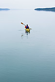 Female sea kayaker paddling pristine waters of Muir Inlet, overcast sky in distance, Glacier Bay National Park, Alaska