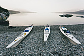 Three sea kayaks pulled up into shoreline of secluded cove in Muir Inlet, overcast sky in distance, Glacier Bay National Park, Alaska