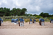 Ostseestrand mit Blick in Richtung Wälder mit blau weißen Strandkörben und bewölktem Himmel, Usedom, Mecklenburg-Vorpommern, Deutschland
