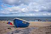 Old fishing boat on the beach in Bansin. Windy day with slightly wavy cloudy sky and tents on the beach, Usedom, Mecklenburg-Western Pomerania, Germany