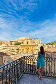 Young woman admiring from an elevated terrace St Peter church, Modica, Ragusa province, Sicily, italy