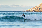 Mann beim Surfen am Strand von Unstad im Winter. Vestvagoy, Nordland, Nordnorwegen, Norwegen