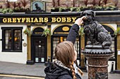 United Kingdom, Scotland, Edinburgh, listed as World Heritage, Tourist touching Bobby's nose in front of the Greyfriars Bobby's Bar