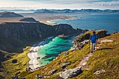 HIKER AT THE SUMMIT OF MOUNT MATIND ABOVE THE WHITE SAND BEACHES AND TURQUOISE WATERS OF THE ISLAND OF ANDOYA, NORWAY