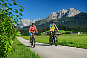 Man and woman cycling with Kaiser Mountains in the background, Kaiser Mountains, Tyrol, Austria