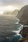 Steep coast in the west of the island of Vágar with the waterfall Bøsdalafossur and the rock needle Geitaskoradrangur near the largest lake in the Faroe Islands, Leitisvatn, Faroe Islands