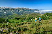 Man and woman hiking with Picos de Europa in the background, from Picu Tiedu, Picos de Europa, Picos de Europa National Park, Cantabrian Mountains, Asturias, Spain
