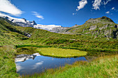 High fence and black wall are reflected in mountain lake, Eye of God, Venediger Group, Hohe Tauern, Hohe Tauern National Park, East Tyrol, Austria