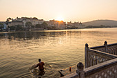 Baden am frühen Morgen in Pichola Lake mit Blick auf City Palace, Udaipur, Rajasthan, Indien