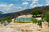 Menschen, die in dem künstlichen Pool baden, der mit Wasser aus Süßwasserquellen gefüllt ist, deren Wasser mit Kalziumkarbonat und anderen Mineralien in Hierve el Agua in der Nähe von Oaxaca, Südmexiko, übersättigt ist.