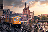 Panoramablick der Berliner U-Bahn mit Oberbaumbrücke im Hintergrund im goldenen Abendlicht bei Sonnenuntergang. Bezirk Friedrichshain-Kreuzberg, Berlin, Deutschland
