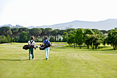 Freunde, die Golftasche tragen, gehen auf Golfplatz
