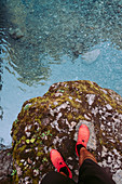 Männerbeine in Sportschuhen, die auf Felsen durch Strom stehen