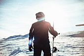 Silhouette of a person wearing a black ski suit, helmet and goggles holding a snowboard standing on top of a snowy slope.