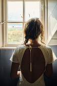 Rückansicht, eine Frau in einem weißen Kleid durch ein Fenster.