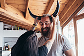 Woman holding cow horns onto head of smiling bearded man with brunette hair.