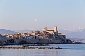 France, Alpes-Maritimes, Antibes, Point of the îlette, old Antibes and his ramparts Vauban, both saracen towers of the castle Grimaldi with in background the Alps of the South covered with snow