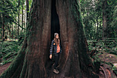 Woman standing in tree hollow in forest,Cathedral Grove,British Columbia,Canada