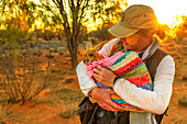 Tourist man holding orphaned baby kangaroo at sunset in Australian Outback, Red Center, Northern Territory, Australia, Pacific