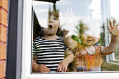 Portrait of toddler girl (2-3) and baby boy (18-23 months) standing behind window