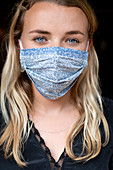 Portrait of young blond woman wearing blue face mask.