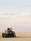 Ein Mann steht auf einem Geländewagen, der auf den Makadikadi-Salzpfannen in Botswana geparkt ist