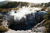 View into a crater with geothermal heat steam rising from the water