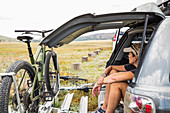 Adult woman sitting on the tailgate of an SUV looking at vista