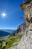 Woman climbs on overhanging ladder on adventure via ferrata Gemmi, Leukerbad and Valais Alps in the background, Gemmi, Bernese Alps, Valais, Switzerland