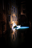Blick auf ein beleutetes Boot und Fische in einem Kanal in San Marco bei Nacht, Venedig, Venetien, Italien, Europa