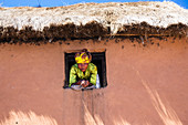 Woman looks out of the window, village in the highlands of Madagascar, Africa