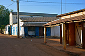 Gambia; Central River Region; Kuntaur; Main street with shops; a man is sitting in his shop in the back building; Chicken runs on the street