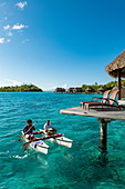 Frühstück wird mit einem Pirogue Auslegerkanu zu einem Überwasserbungalow des Sofitel Bora Bora Private Island Resorts in der Lagune von Bora Bora gebracht, Bora Bora, Leeward Islands, Französisch-Polynesien, Südpazifik