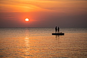 Silhouette von jungem Paar das bei Sonnenuntergang auf einer Badeplattform vor dem Ong Lang Beach steht, Ong Lang, Insel Phu Quoc, Kien Giang, Vietnam, Asien