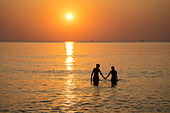 Silhouette of a romantic young couple holding hands in the water in front of Ong Lang Beach at sunset, Ong Lang, Phu Quoc Island, Kien Giang, Vietnam, Asia