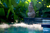 Morgendunst auf der Oberfläche eines Pools mit einer Hindu-Statue an der Seite. Bali, Indonesien, Asien