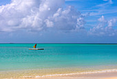 A woman with a bright yellow sarong, standing on a float, off a beach, agains a turqoise sea. Shot in Antigua.