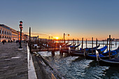 Gondolas in front of Riva degli Schiavoni with sunrise in the background in Venice, Veneto, Italy