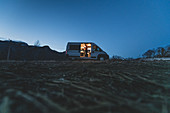 Silhouette vom Camper Van abends auf einem Hügel mit eingeschalteten Lichtern und Mann, der an der offenen Seitentür stehend