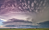 A massive tornado super-cell with mammatus, arcus, tail cloud, and wall cloud, illuminated at sunset with pink and blue colours