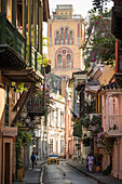 Blick entlang der engen Straße in die Altstadt, elegante historische Häuser mit Balkon und hohem Kirchturm