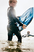 Porträt des Jungen, der Nassanzug trägt, Surfbrett in Ozean trägt, Santa Barbara, Kalifornien, USA.