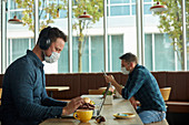 Zwei Männer sitzen in einem Café und arbeiten mit einem Laptop und einem Smartphone aus der Ferne